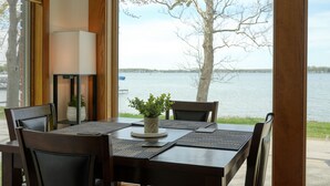 Une table à manger avec des chaises, une plante en pot et une vue sur un lac, visible à travers de grandes fenêtres.