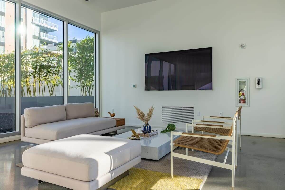 A modern living room with a large window, a flat-screen TV, a sofa, a coffee table, and a side table.