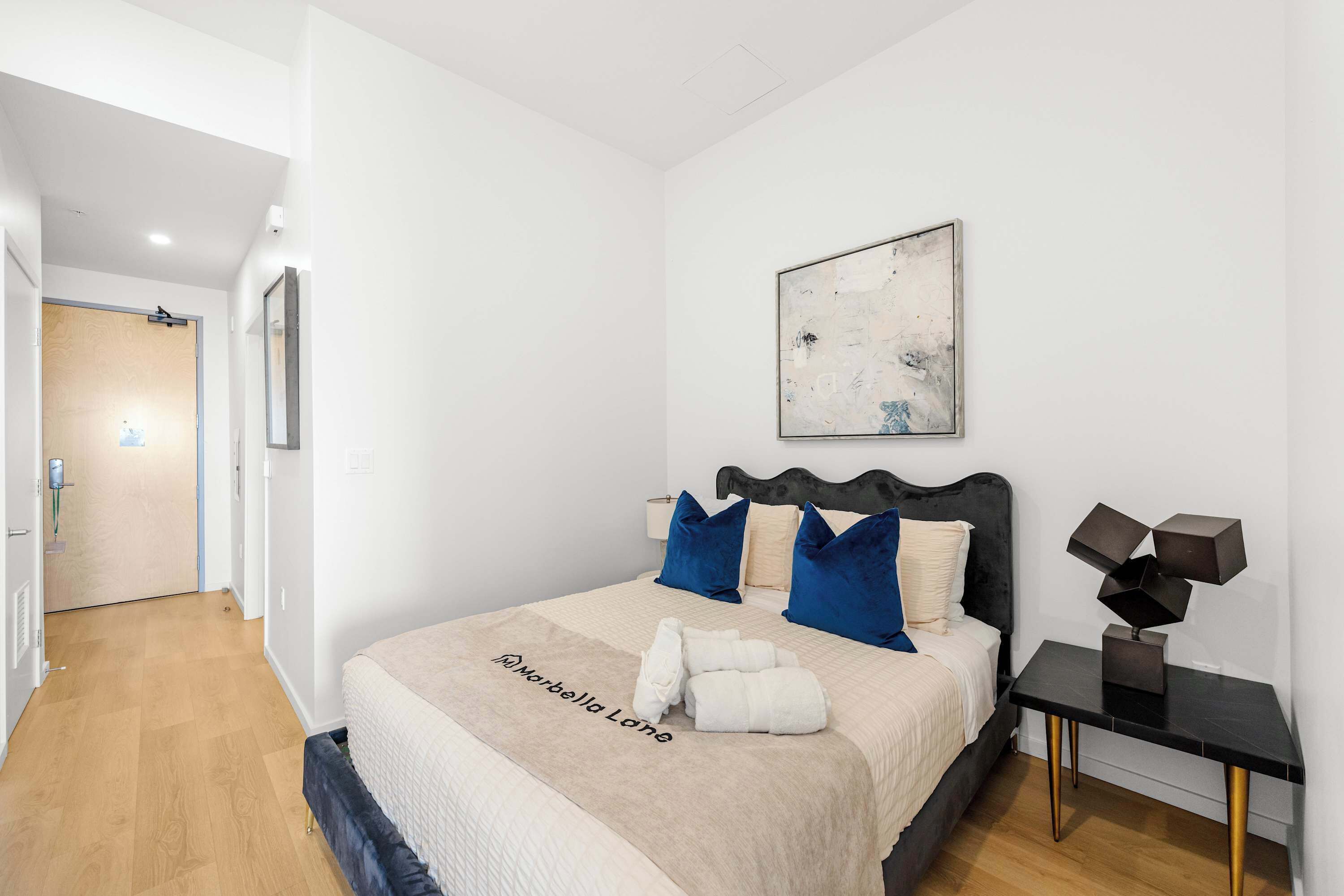 A modern bedroom with a bed, bedside table, and a painting on the wall.