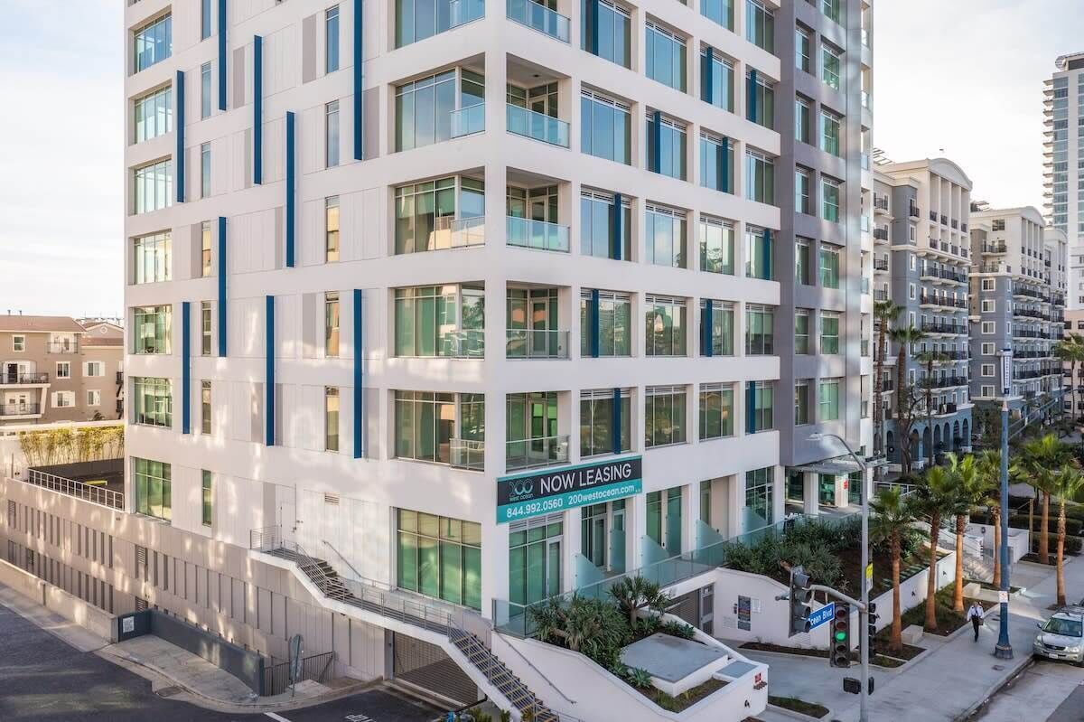 A multi-story building with a 'NOW LEASING' sign, large windows, and a modern design.