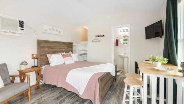 A bedroom with a wooden bed, a desk with a chair, a TV mounted on the wall, and a window with curtains.