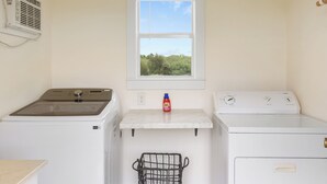 A laundry room with a window, a wall-mounted air conditioner, and two washing machines.