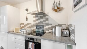 A modern kitchen with a built-in oven, a stainless steel range hood, and a tiled backsplash. - Ardtornish Apartment (Tayvallich)