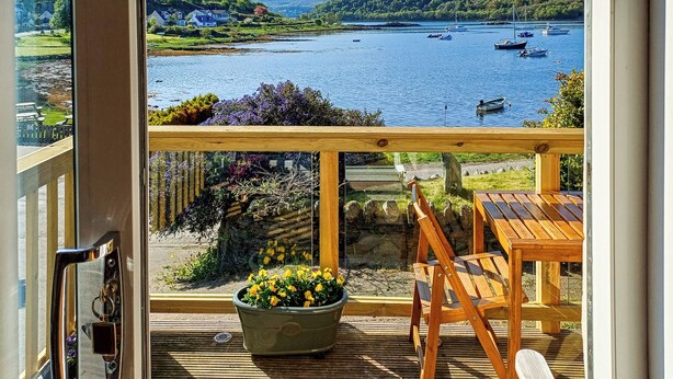 A balcony with a view of a lake, boats, and a distant hill. - Ardtornish Apartment (Tayvallich)