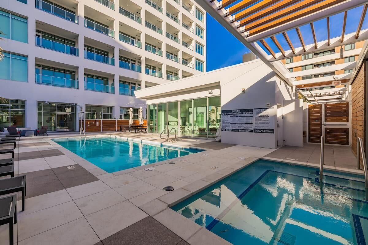 A hotel pool area with a large pool, sun loungers, and a building with multiple balconies.