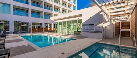 A hotel pool area with a large pool, sun loungers, and a building with multiple balconies.