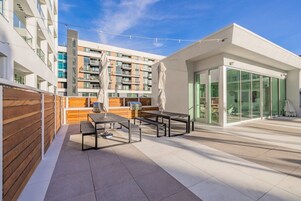 Un patio exterior moderno con valla de madera, una parrilla para barbacoa y un área de comedor con paredes de vidrio.