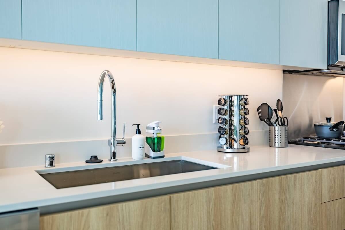 A modern kitchen with a stainless steel sink, a built-in oven, and a variety of kitchen utensils and appliances.