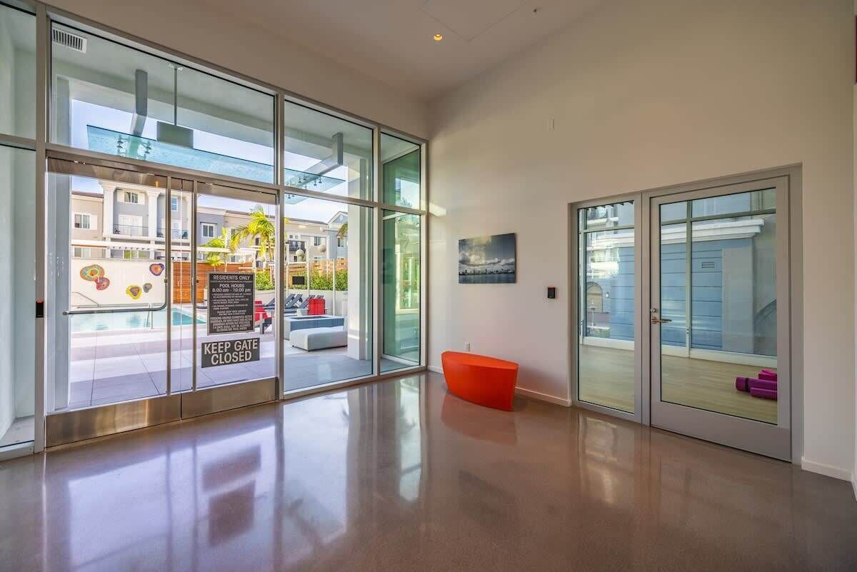 A modern hotel lobby with large glass doors, a red bench, and a view of the outside buildings.