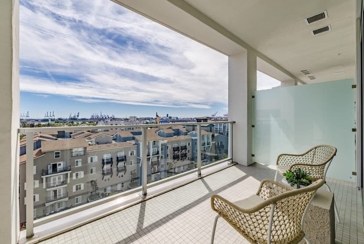 Un balcon donnant sur des immeubles d’habitation, avec une balustrade en verre et des fauteuils en osier.