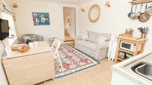 Eine kompakte Küche mit Mikrowelle, Spüle und hängenden Töpfen. Es gibt einen Essbereich mit Tisch und Stühlen, ein Sofa und einen gemusterten Teppich.