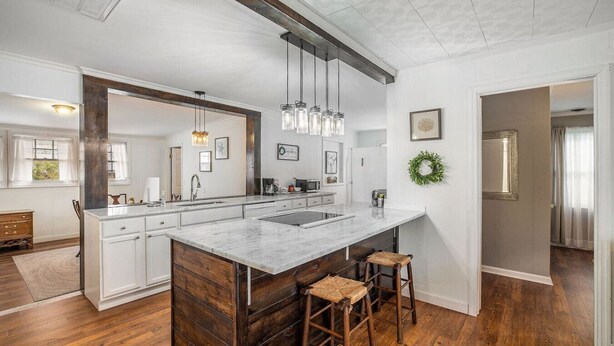Una cocina moderna con una isla grande, taburetes de madera, luces colgantes y vistas al área de comedor contigua.