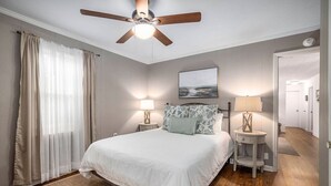 Un dormitorio con cama, dos mesitas de noche, ventilador de techo y un cuadro en la pared.