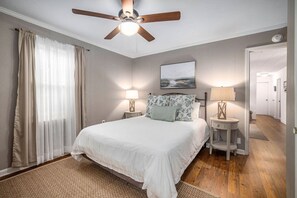 A bedroom with a bed, two bedside tables, a ceiling fan, and a painting on the wall. - Cheerful 4br/1.5ba Farmhouse Close to Shem Creek! (Mount Pleasant)