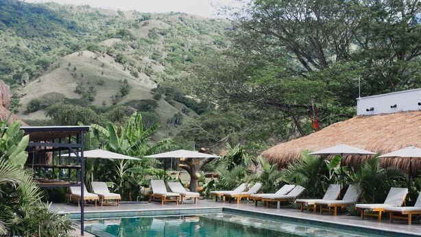 A clear blue pool with lounge chairs and umbrellas, surrounded by lush greenery and hills. - Anzalik Hotel Boutique (Anza)