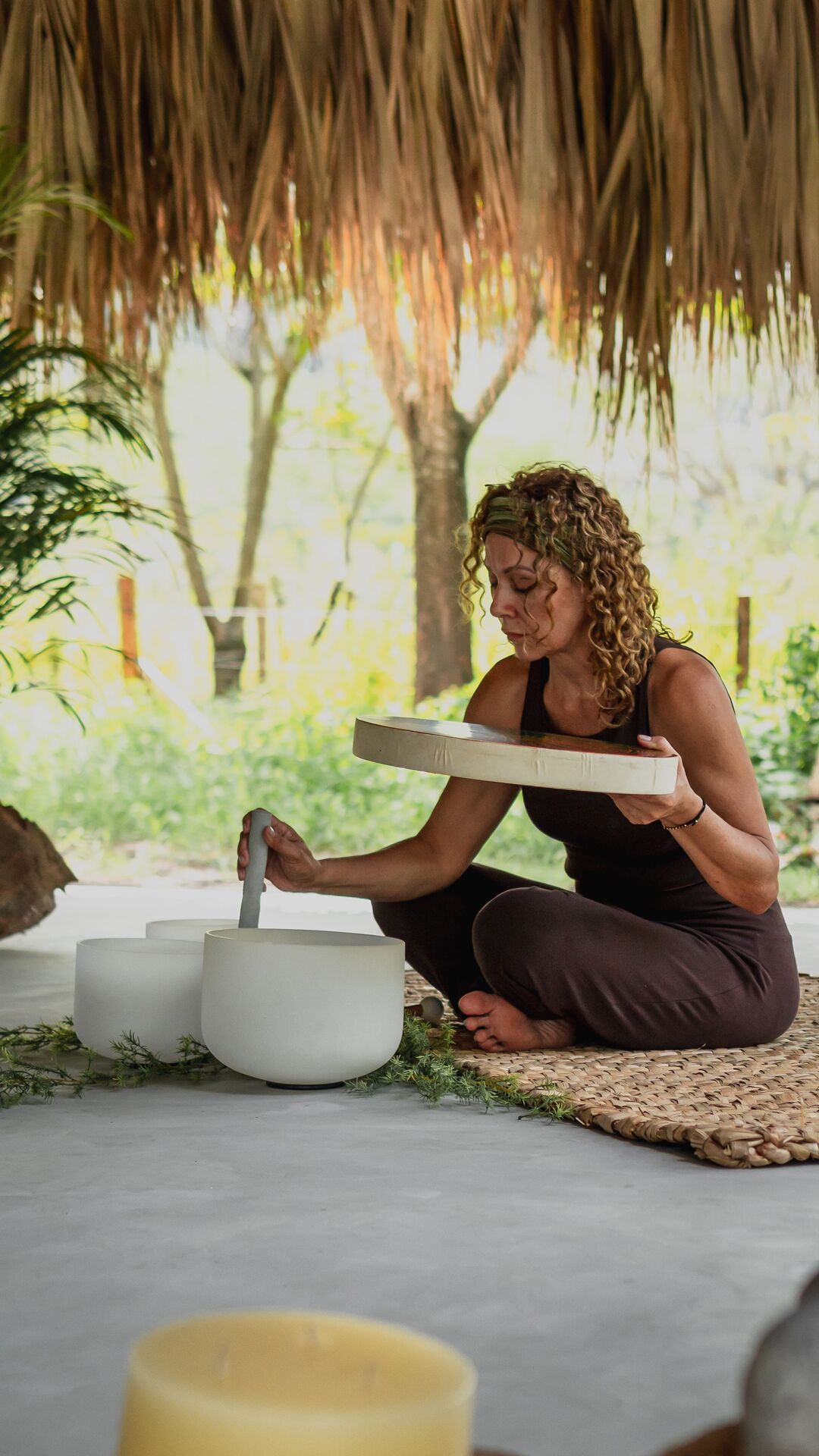 Uma pessoa sentada num tapete, segurando um livro e uma tigela, com várias tigelas e uma chávena no chão.