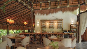 A restaurant with a rustic thatched roof, wooden furniture, and a bar area with shelves of bottles and glasses. - Anzalik Hotel Boutique (Anza)