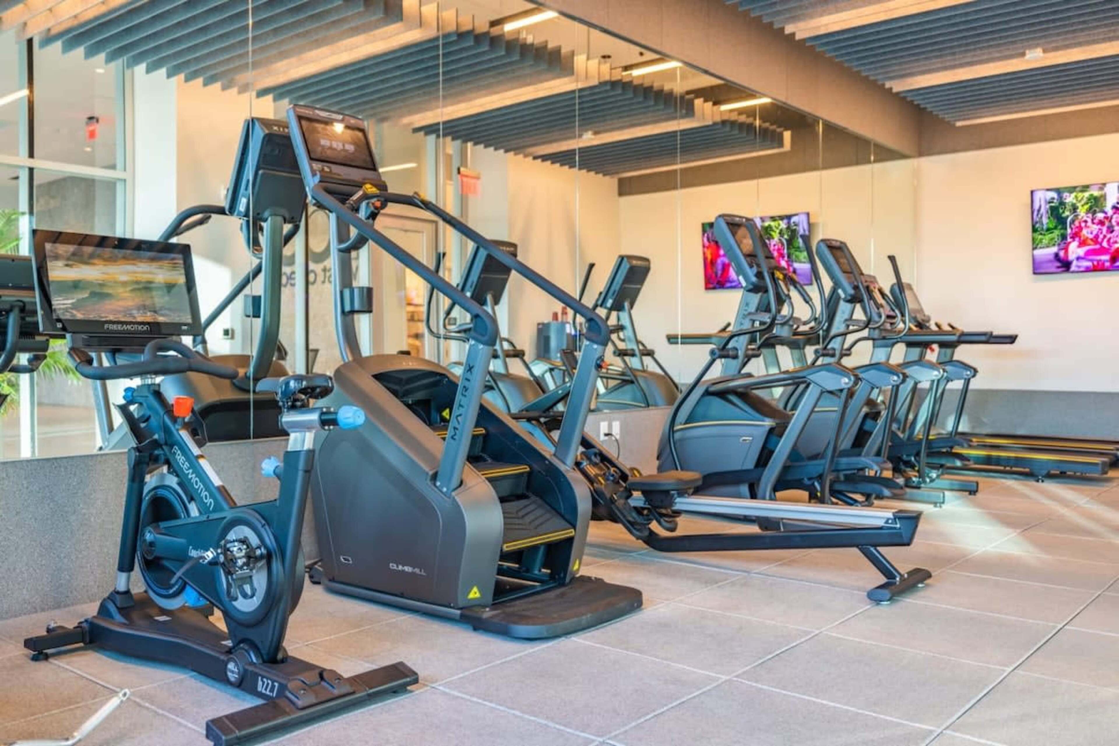 A modern gym with various cardio machines, including treadmills and stationary bikes, arranged in a spacious layout.