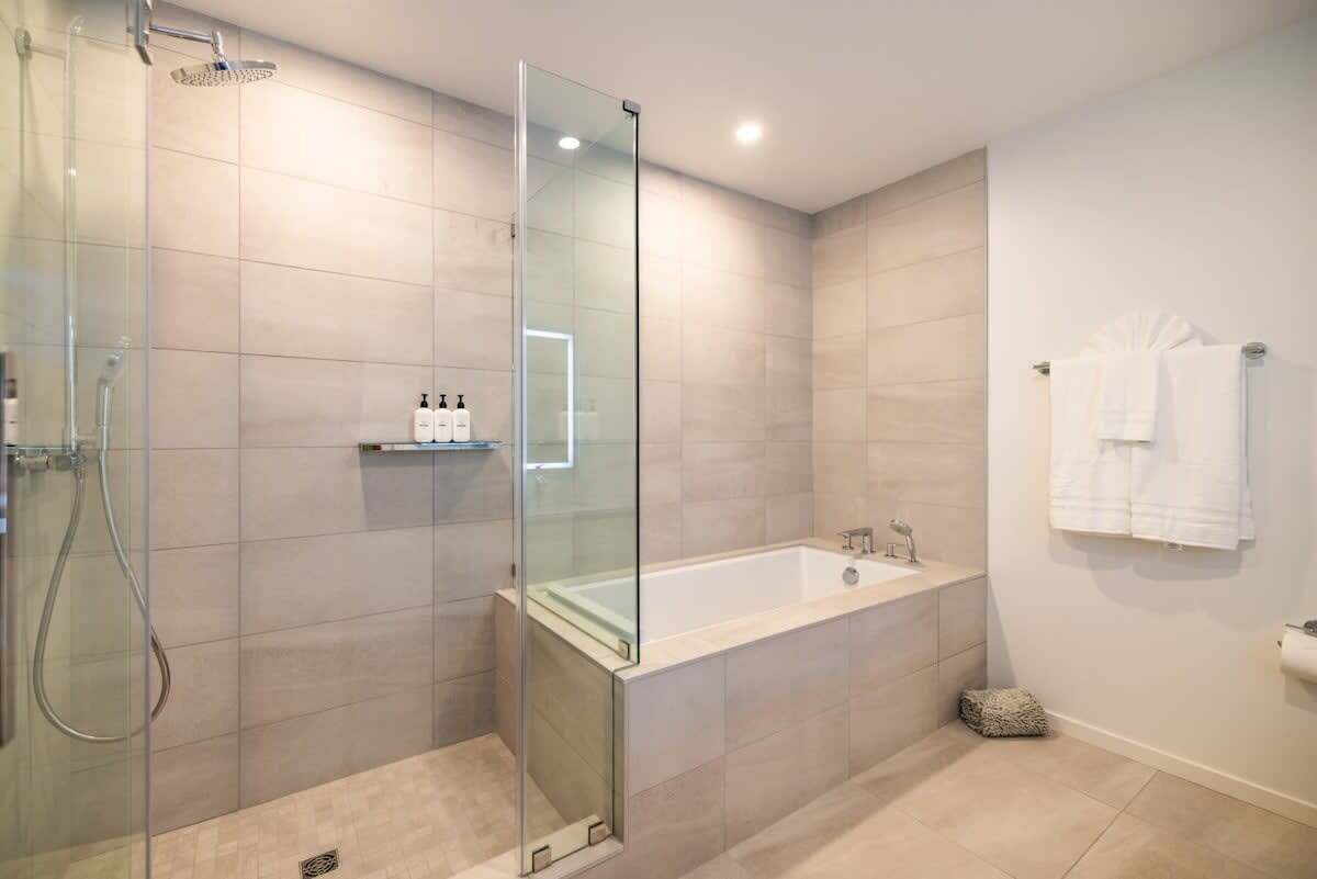 Un baño moderno con ducha de vidrio, una bañera independiente y un perchero blanco.