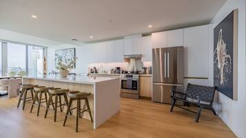 A modern kitchen with a central island, bar stools, stainless steel appliances, and a large window providing natural light.