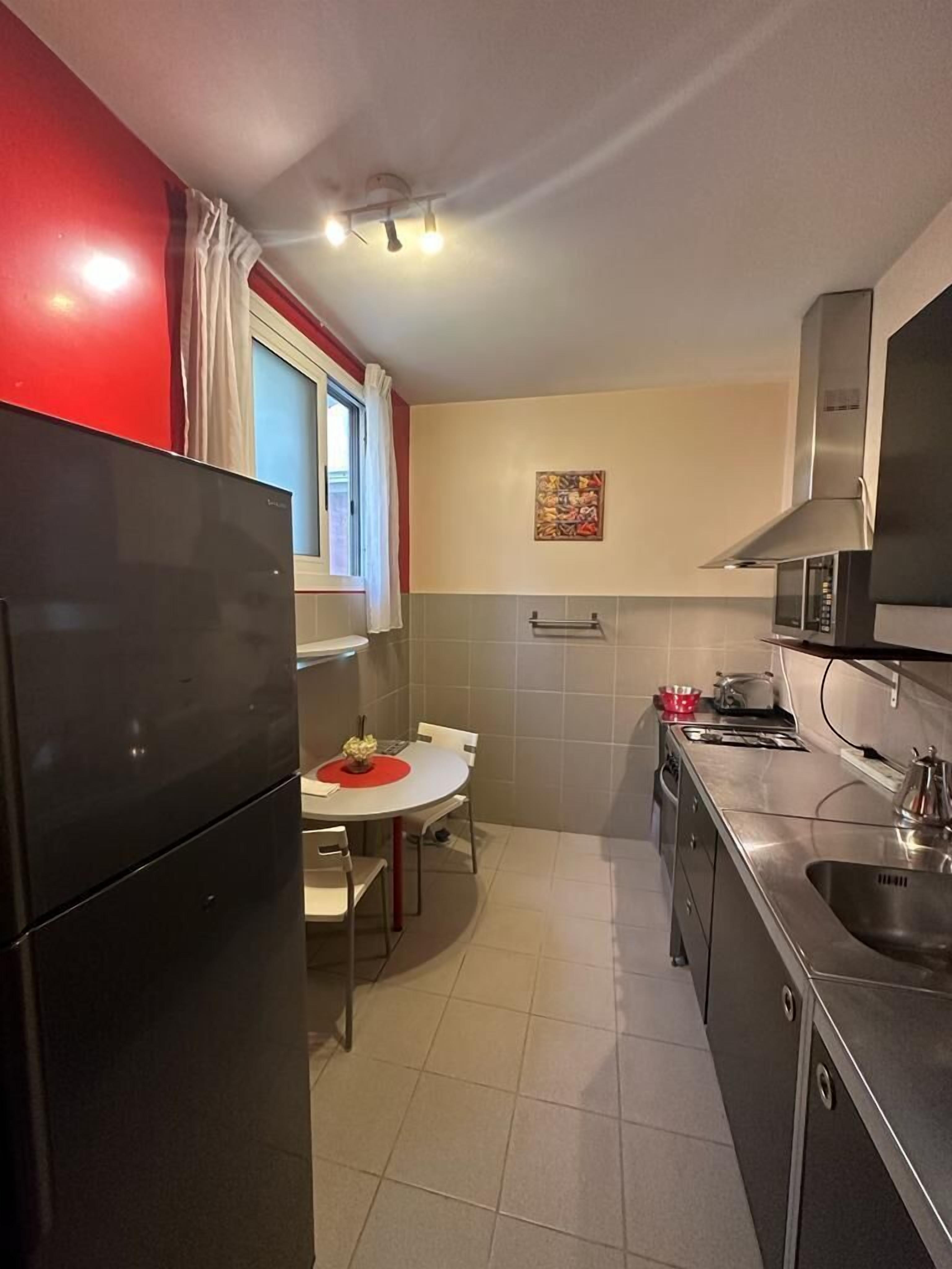 A compact kitchen with a refrigerator, a dining table with chairs, a microwave, and a sink.