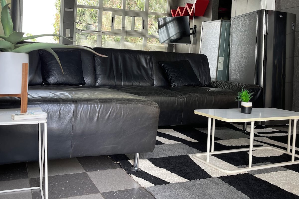 Un salon moderne avec un canapé en cuir noir, une petite table blanche et un tapis à carreaux noirs et blancs.