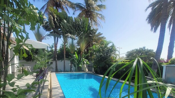 A rectangular swimming pool surrounded by lush greenery and palm trees. - Villa Anna Dakar (Dakar)