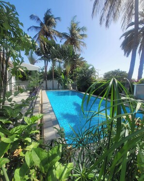 A rectangular swimming pool surrounded by lush greenery and palm trees. - Villa Anna Dakar (Dakar)