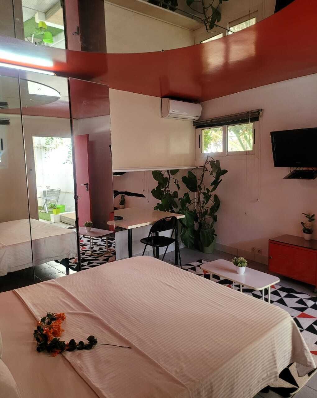 A room with a bed, a desk, a chair, a TV, and a potted plant.