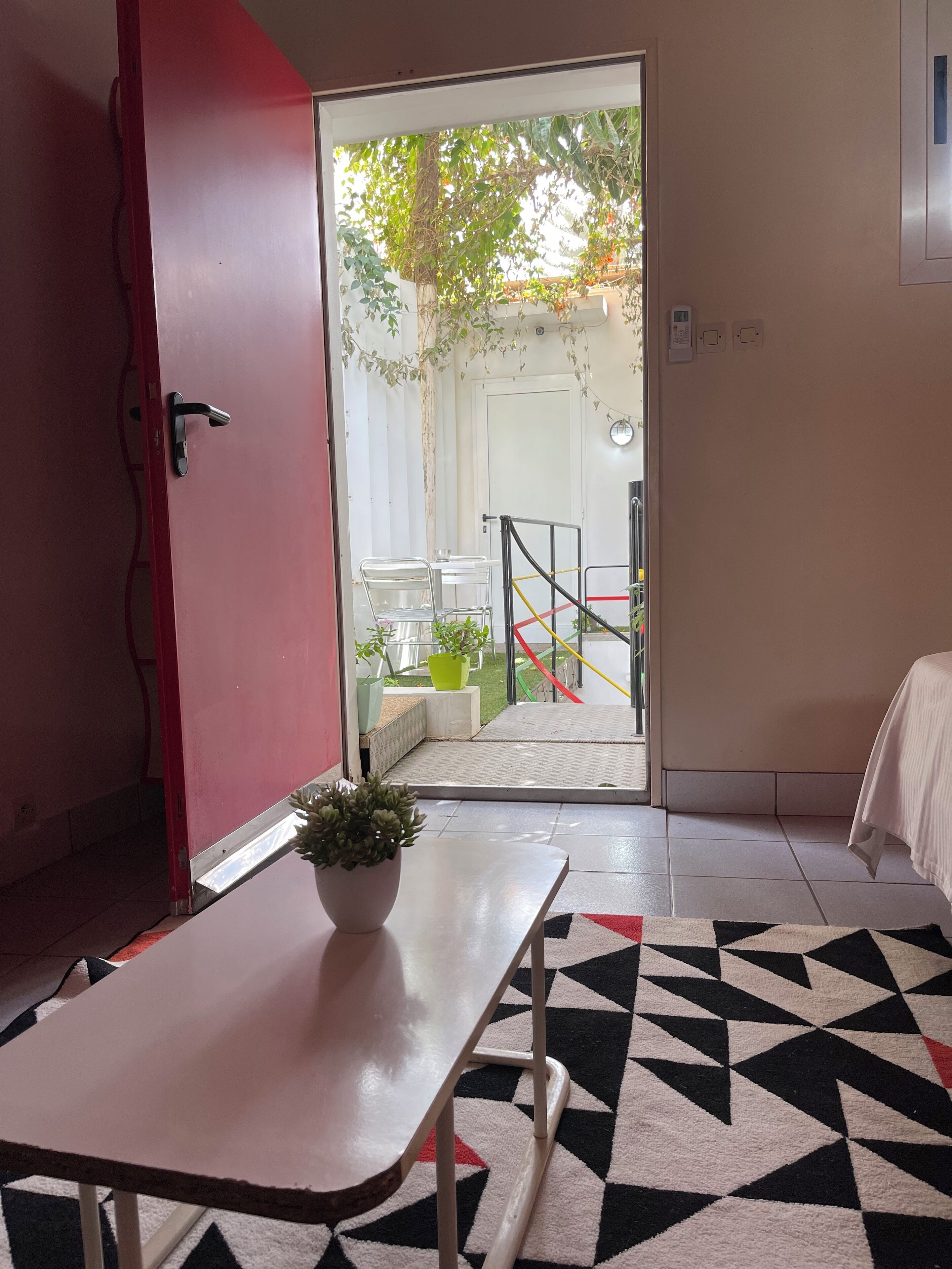 Una habitación con una puerta roja, una mesa blanca con una planta en maceta y un tapete de diseño geométrico.