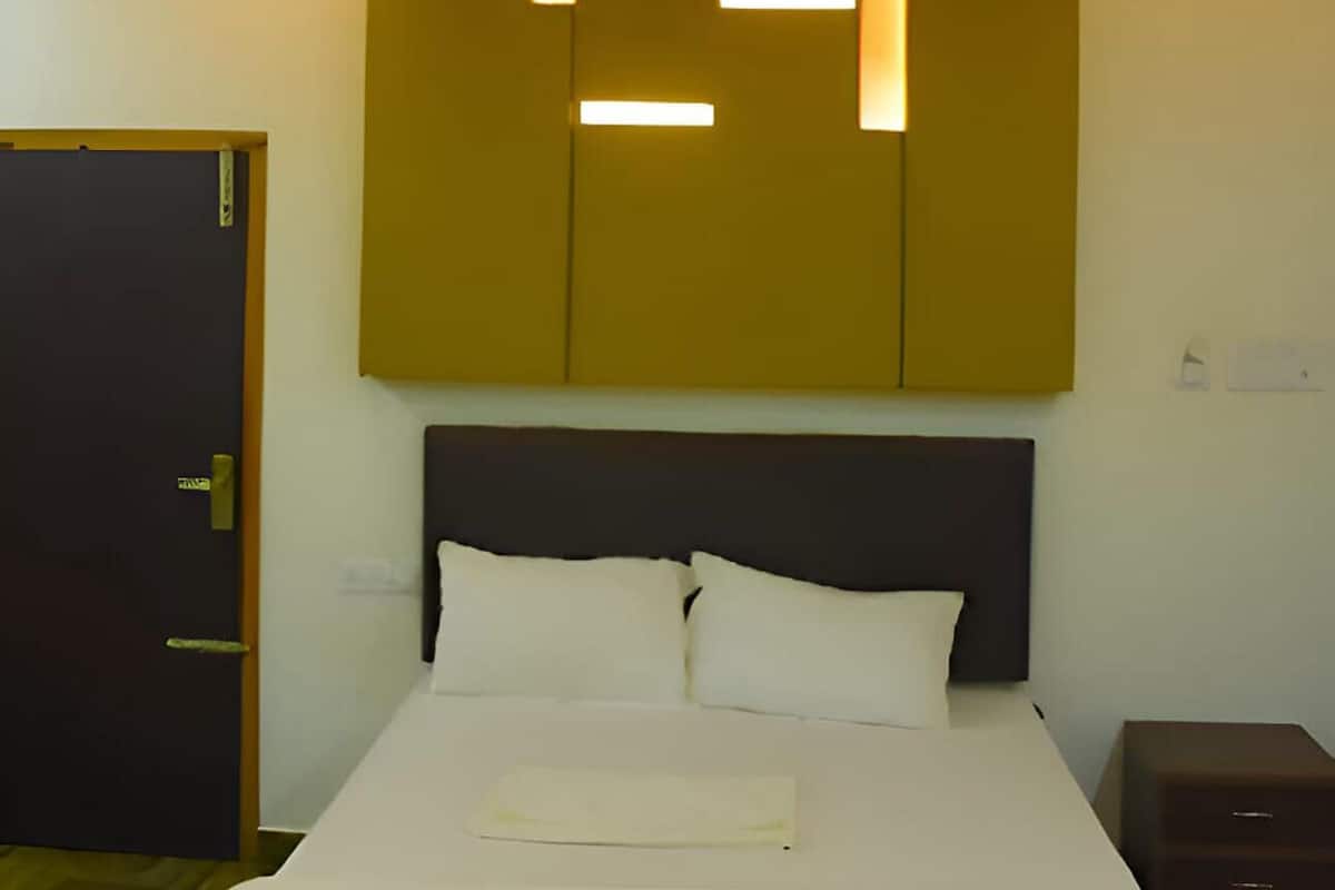 Una habitación de hotel con cama, ventilador de techo y lámpara fijada a la pared.