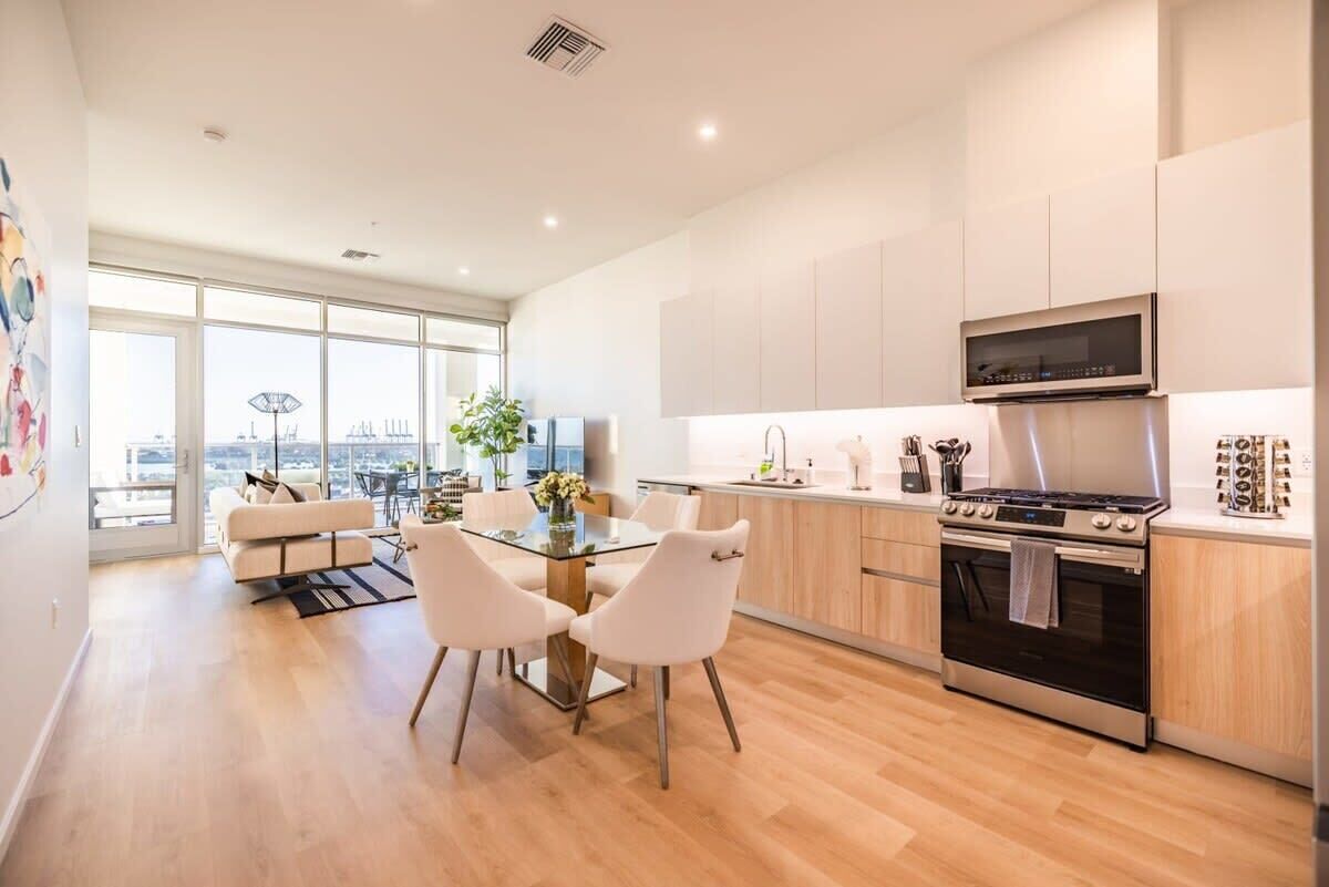 A modern kitchen with a dining area, large windows, and a city view.