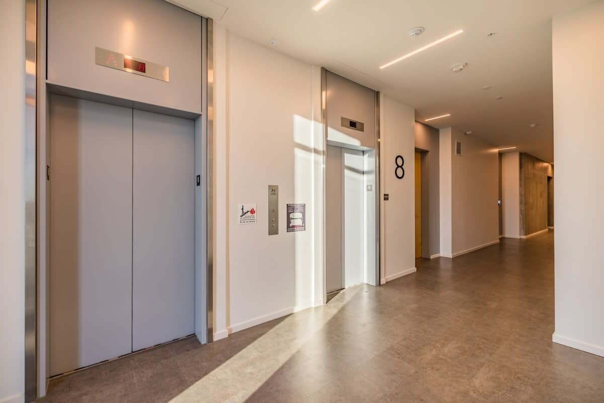 A modern hallway with two elevators, a fire alarm, and a number 8 sign.