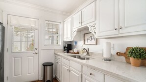 A kitchen with white cabinets, a stainless steel sink, a coffee maker, and a potted plant.