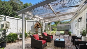 A covered patio area with wicker furniture, a pergola, and a brick floor.