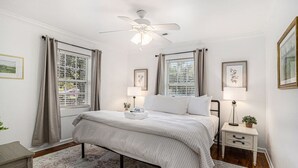A bedroom with a bed, bedside tables, a ceiling fan, and window treatments.
