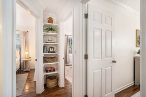 A hallway with a white door, a shelf unit with baskets, and a small table with a lamp.