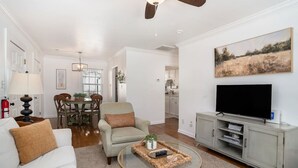 A living room with a ceiling fan, a TV, a sofa, a coffee table, and a dining area with chairs and a table.