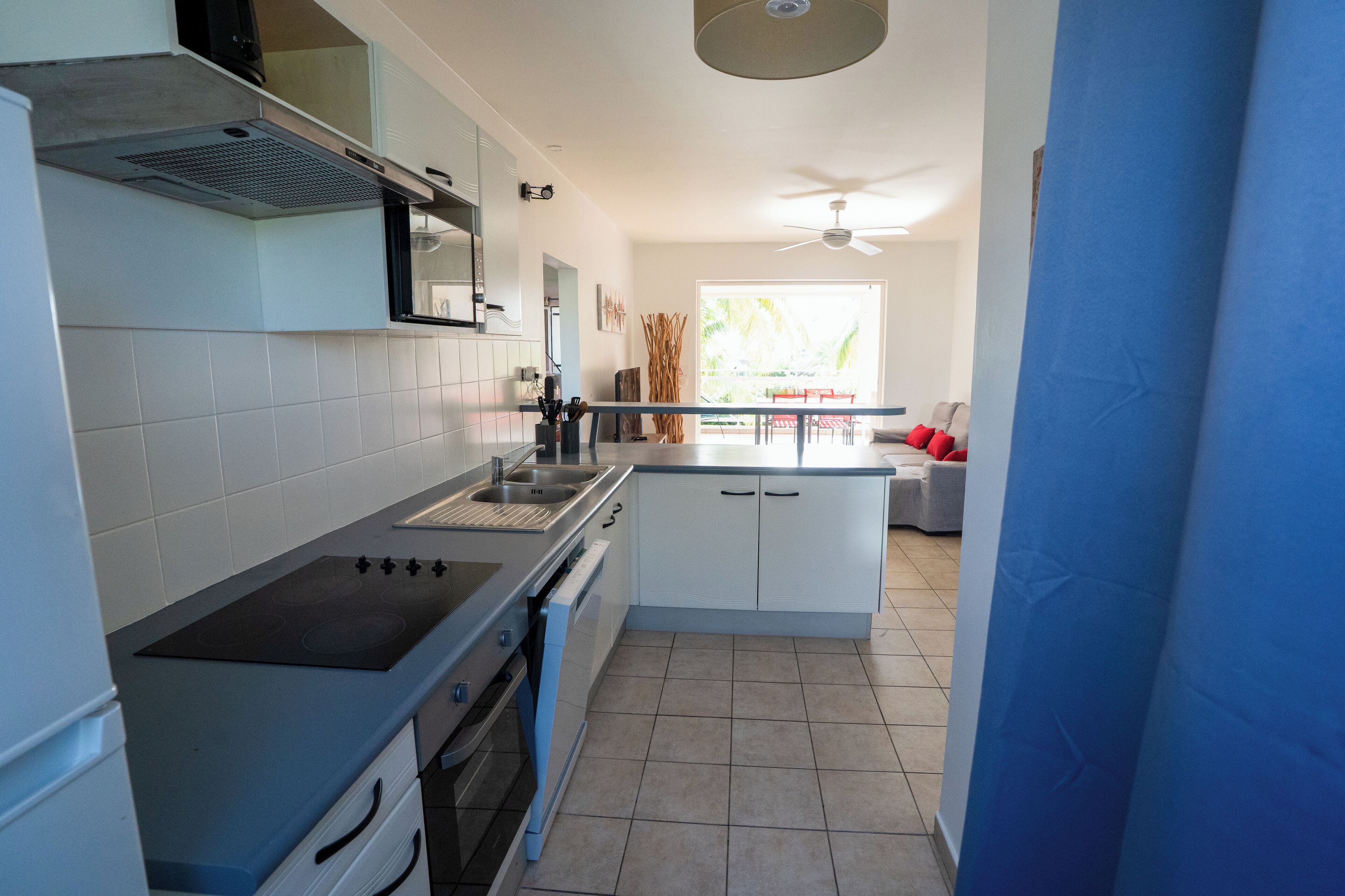 A modern kitchen with a stove, oven, and sink. There is a dining area with a table and chairs visible through an open door.