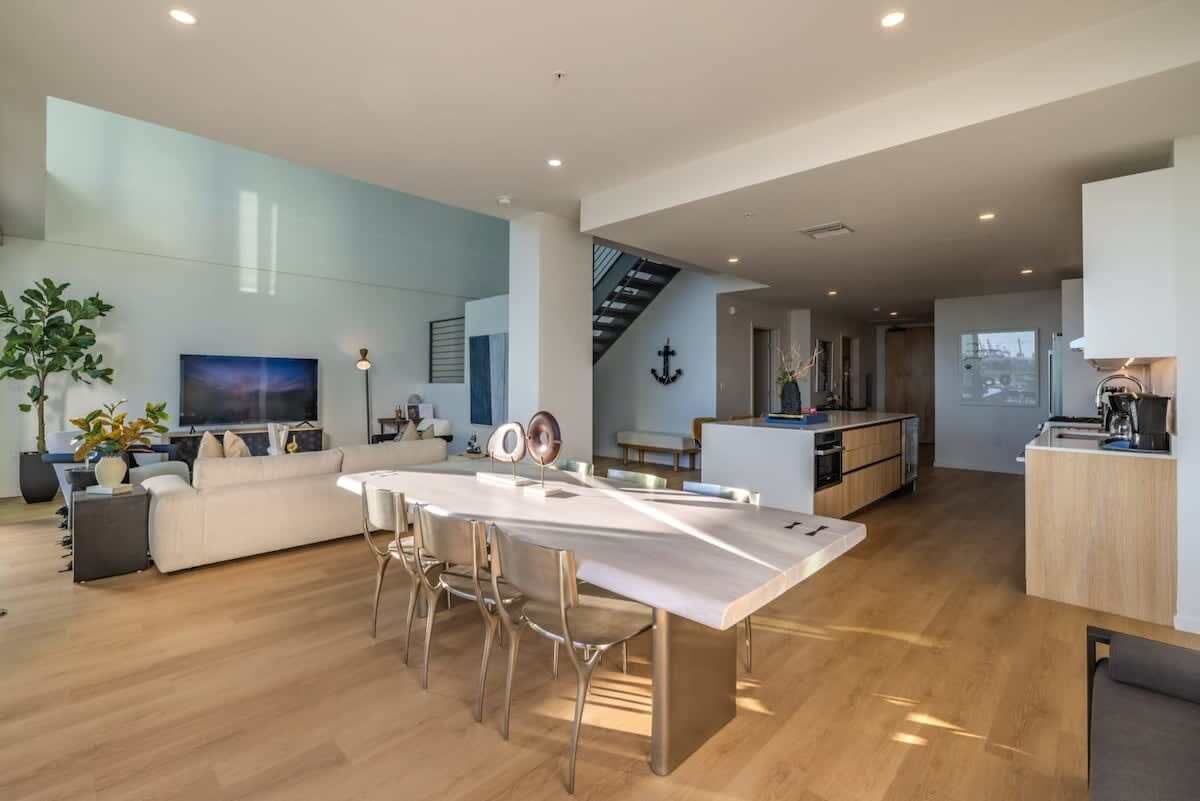 A modern open-plan living and dining area with a kitchen, a staircase, and a large window.