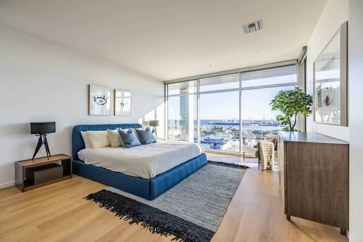 A modern bedroom with a large bed, a view of the city, and a large window.
