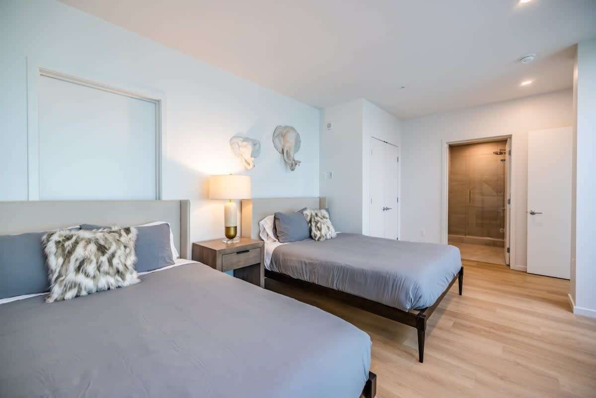 A bedroom with two beds, a nightstand with a lamp, and a door leading to a bathroom.