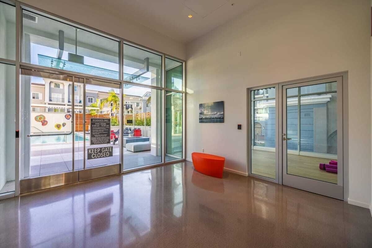 A modern hotel lobby with large glass doors, a red bench, and a view of the pool area.