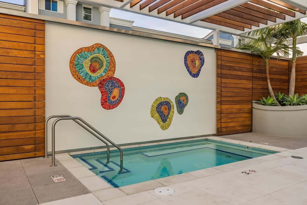 Una piscina con cubierta de madera y un muro decorado con mosaicos de colores.