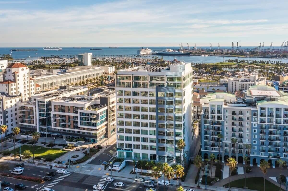 A high-rise hotel with multiple floors, a central courtyard, and a view of the marina and port in the background.