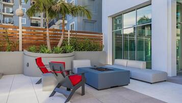 A modern outdoor seating area with a fire pit, a palm tree, and a view of a high-rise building.