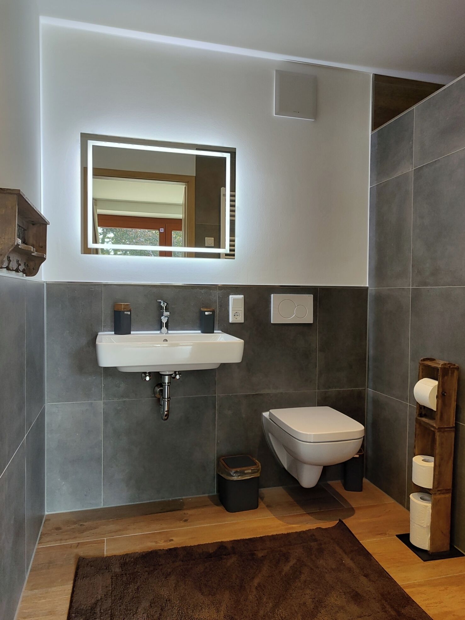 Une salle de bain moderne avec un lavabo blanc, un bidet et une étagère en bois où est posé du papier toilette.