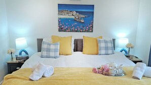 Une chambre d’hôtel avec un lit, des oreillers, une table de chevet, une lampe, un tableau et un plateau avec des serviettes et des fleurs.