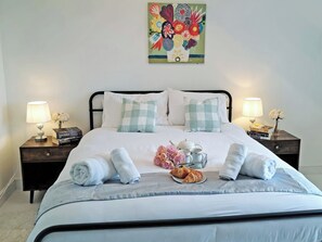 A neatly made bed with pillows, a bedside table with a lamp, a vase with flowers, and a painting on the wall. - 6 bedroom accommodation in Stonea, near Ely (Stonea, near Ely)