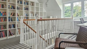 Une bibliothèque avec des étagères, un escalier, une chaise et une table.